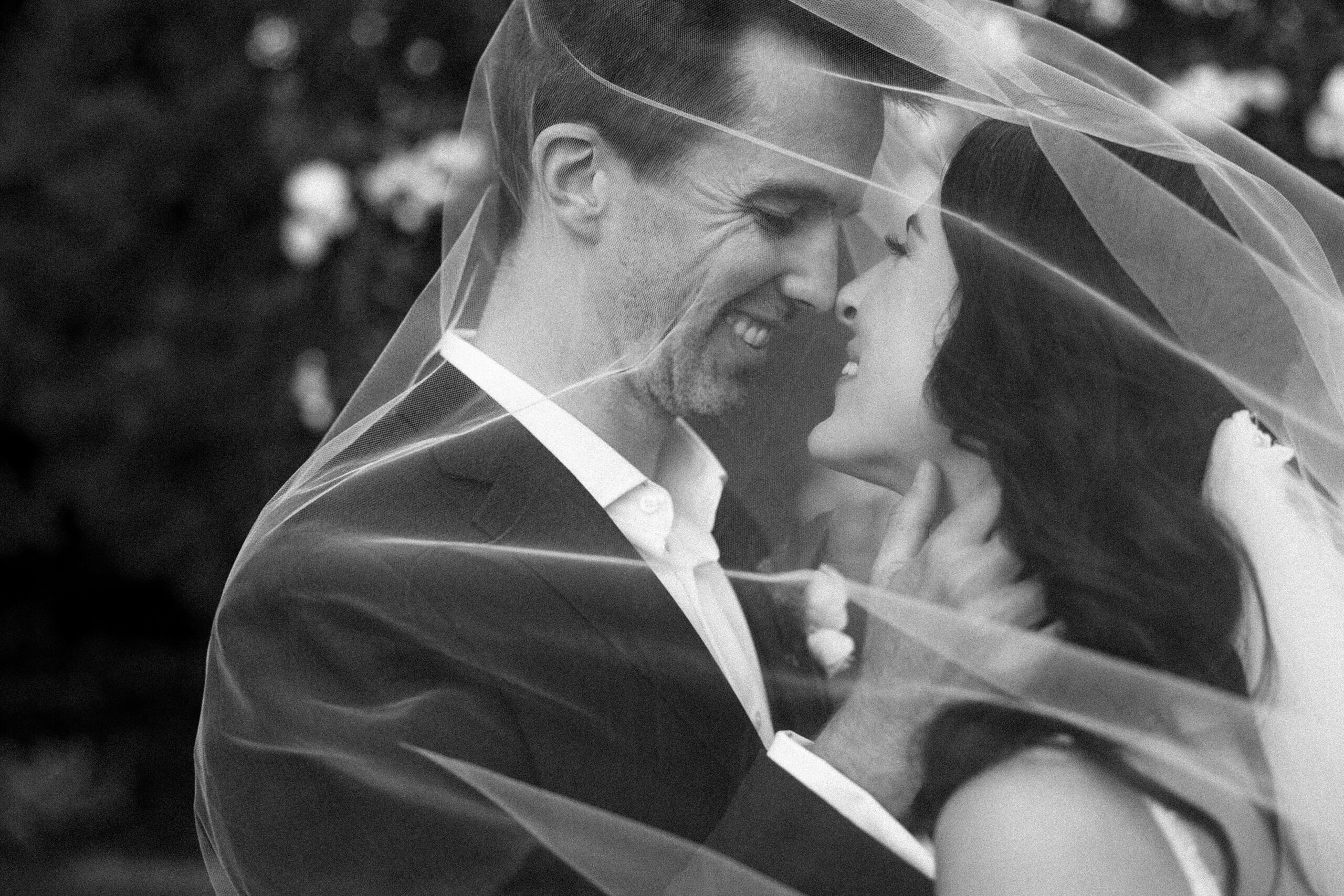 A bride and groom share a romantic moment under a delicate veil, capturing their love and joy on their wedding day.