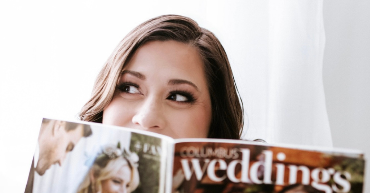 Heather Arra, owner of Girasole & Co. Weddings, playfully peeks behind a Columbus wedding magazine, showcasing her enthusiasm for wedding planning and local inspirations.