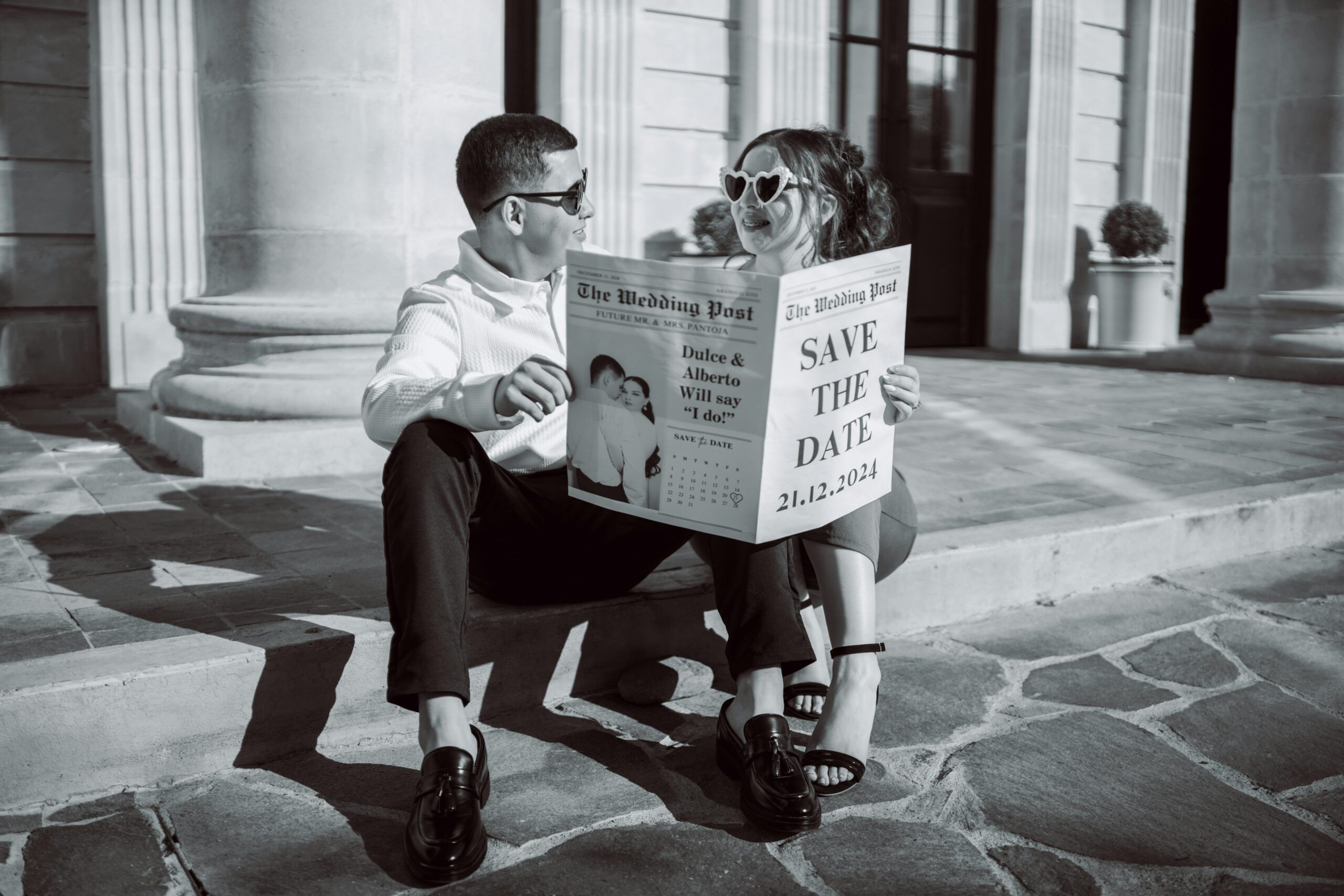 Couple holding a newspaper with their wedding date displayed, smiling as a creative save-the-date announcement.