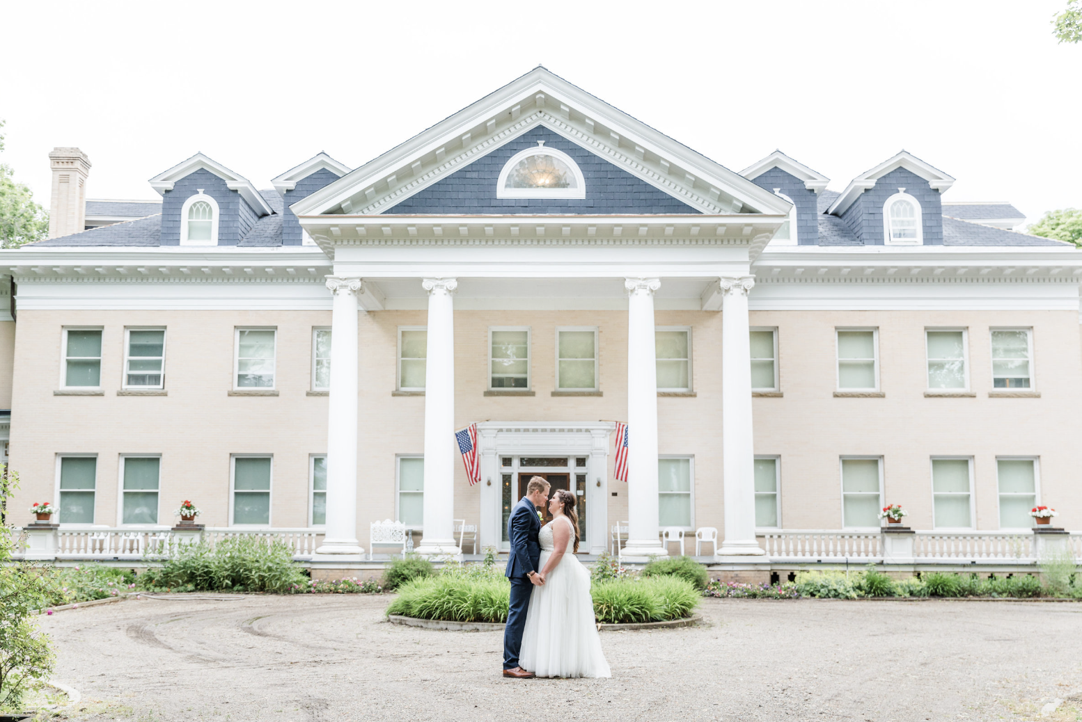 Couple standing hand in hand in front of wedding venue, smiling.